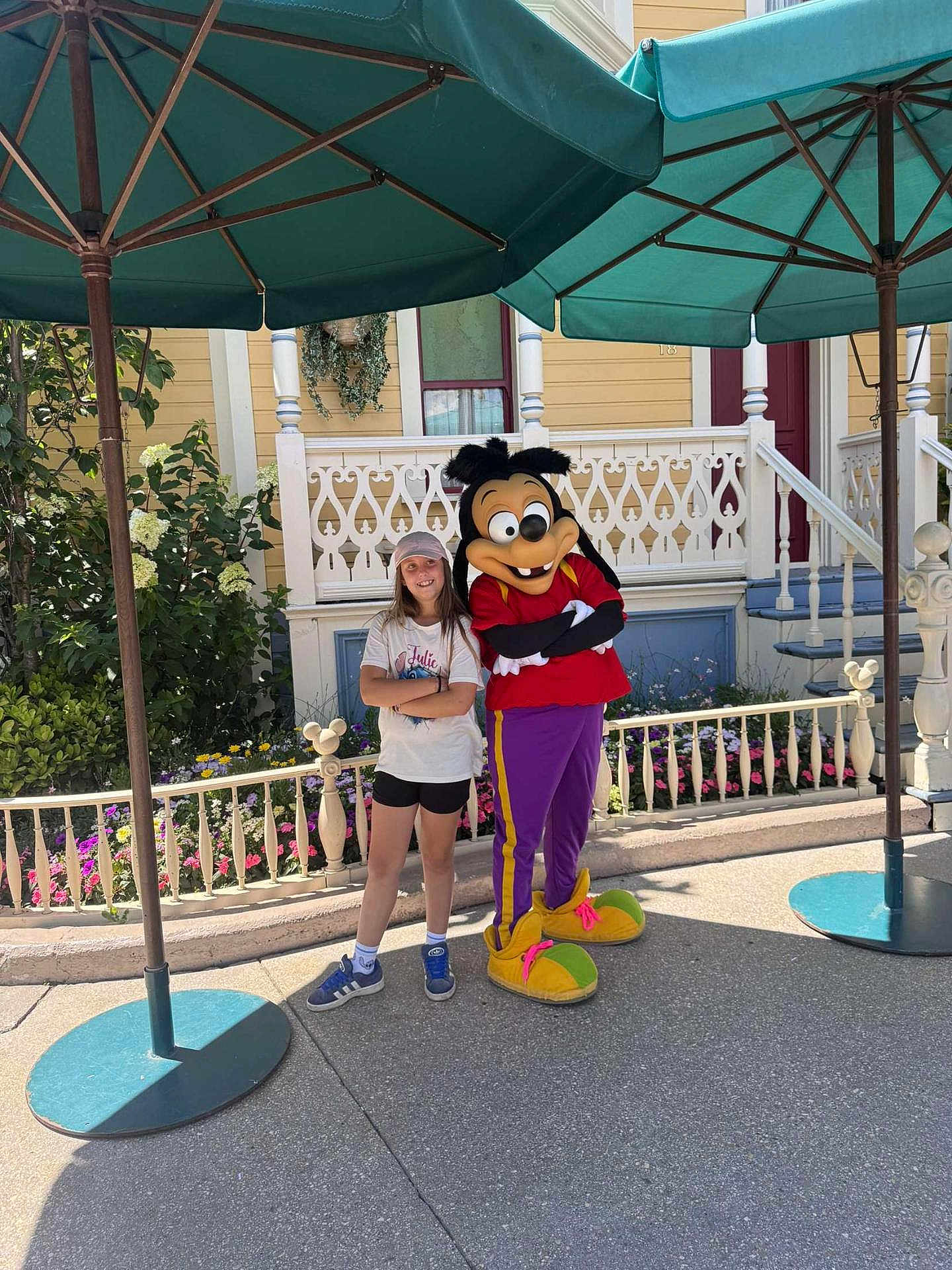 Julie a rejoint le concours — aidez-le/la à gagner de superbes lots ! child, person, costume, cartoon_character, umbrella, outdoor, smile, standing, flowerbed, house, railing, sidewalk, hat, shorts, tshirt, shoes, character, theme_park, daytime, fun