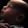 baby, infant, side_profile, face, hand, curious, looking_up, soft_lighting, portrait, close_up, newborn, child, dark_background, expression, skin, person, young, cute, innocence, peaceful