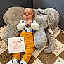 baby, infant, milestone_card, plush_elephant, crocheted_blanket, yellow_pants, white_shoes, smiling, happy, indoors, cute, child, face, clothing, person, toy, comfort, sitting, celebration, portrait