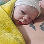 newborn, baby, towel, white_cap, tattoo, skin, sleepy, closeup, infant, person, resting, headwear, blanket, indoors, soft_texture, human, cute, face, newborn_baby, portrait