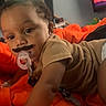 baby, background, child, clothing, curious, cute, expression, face, indoor, infant, lying_down, mustache, orange_blanket, pacifier, person, reaching, room, soft_lighting, toddler, toy