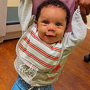 Robert joined the competition — help win amazing prizes! baby, child, smiling, holding_hands, indoor, floor, wooden_floor, clothing, bib, jeans, shoes, person, adult_hands, happy, standing, portrait, human, room, furniture, timestamp