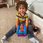 Agustin joined the competition — help win amazing prizes! bed, carpet, casual, child, colorful_blocks, curly_hair, family, floor, home, indoor, jeans, person, playing, relaxed, shoes, sitting, smiling, socks, striped_shirt, toy