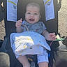 Nathan is registered to the contest to win money with this photo: baby, stroller, blanket, smiling, infant, child, outdoor, sunlight, clothing, foot, hand, toy, seatbelt, warning_label, fabric, cute, happy, person, baby_bib, legs