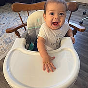 Nathan is registered to the contest to win money with this photo: baby, high_chair, smiling, indoor, wooden_chair, white_tray, flooring, carpet, happy, child, person, clothing, arm, face, hand, furniture, home, cute, infant, seat