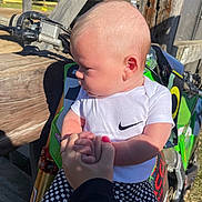 Maddox is registered to the contest to win money with this photo: baby, child, person, hand, holding_hands, outdoor, sunlight, dirt_bike, motorcycle, wood, clothing, white_shirt, checkered_pants, nike_logo, grip, closeup, portrait, nature, daylight, cute
