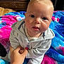 Maddox is registered to the contest to win money with this photo: baby, child, hand, blanket, colorful, blue_eyes, hoodie, white_clothing, indoor, person, infant, cute, soft_texture, tattoo, holding_hand, portrait, face, skin, young_child, curious