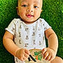 baby, bunny_pattern, child, closeup, crocodile_illustration, curious, cute, fingers, grass, green_background, hand, happy, infant, lying_down, milestone_card, onesie, outdoor, portrait, smiling, young_child