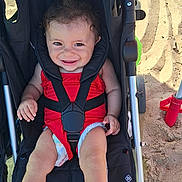Alya a rejoint le concours — aidez-le/la à gagner de superbes lots ! baby, barefoot, beach, child, cute, happy, infant, outdoor, person, playful, portrait, red_outfit, sand, seat, seatbelt, smiling, stroller, summer, sunlight, wheels