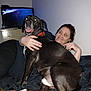 dog, black_dog, person, woman, couch, indoor, hugging, smiling, pet, collar, flash, panting, happy, living_room, blanket, television, furniture, relaxing, night, casual