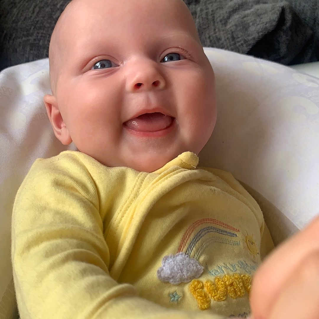 Paisley-Jane is registered to the contest to win money with this photo: baby, blue_eyes, child, closeup, cozy, cute, expression, face, hand_holding, happy, indoor, infant, person, portrait, sitting, skin, smiling, soft_light, texture, yellow_clothing