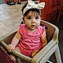 baby, child, high_chair, pink_clothing, headband, bow, indoor, floor_tiles, table, wooden_furniture, face, person, curious, seated, sock, cleaning_tools, broom, dustpan, expression, wide_eyes