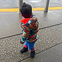 child, toddler, back_view, colorful_jacket, puffer_jacket, hood, boots, pavement, sidewalk, wet, rainy, bollard, parking_lot, tactile_paving, concrete, standing, short_hair, outerwear, cars, urban