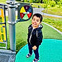 child, boy, playground, outdoor, smiling, jacket, sneakers, grass, trees, spinner, play_equipment, park, happy, person, daylight, casual_clothing, recreation, fun, nature, sport