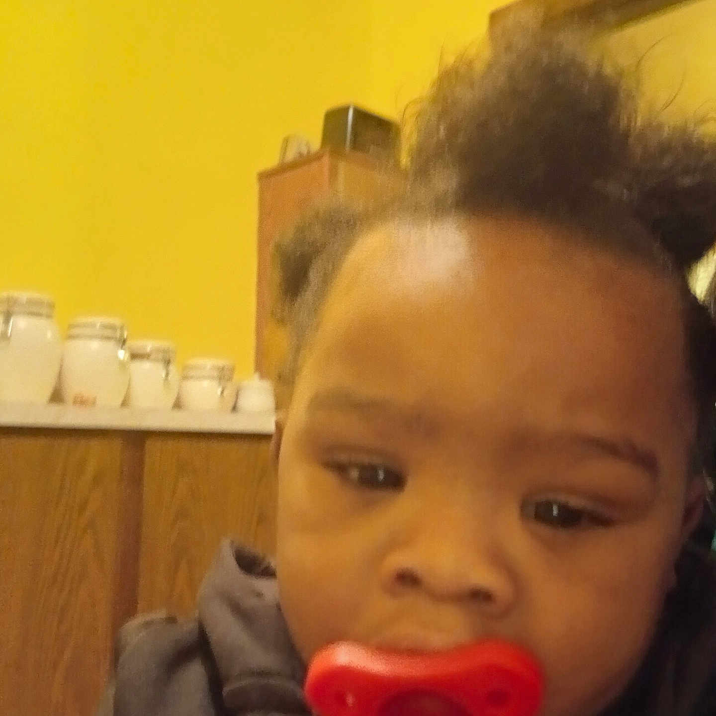 Kayden is registered to the contest to win money with this photo: baby, blur, cabinet, child, closeup, clothing, expression, face, furniture, hair, head, indoor, infant, pacifier, person, portrait, room, wall, yellow, young_child