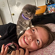 Concrete Gas Station joined the competition — help win amazing prizes! kitten, cat, person, smiling, happy, indoor, bed, pillow, collar, young_person, cute, pet, animal, lying_down, face, hand, furniture, door, bowl, blanket