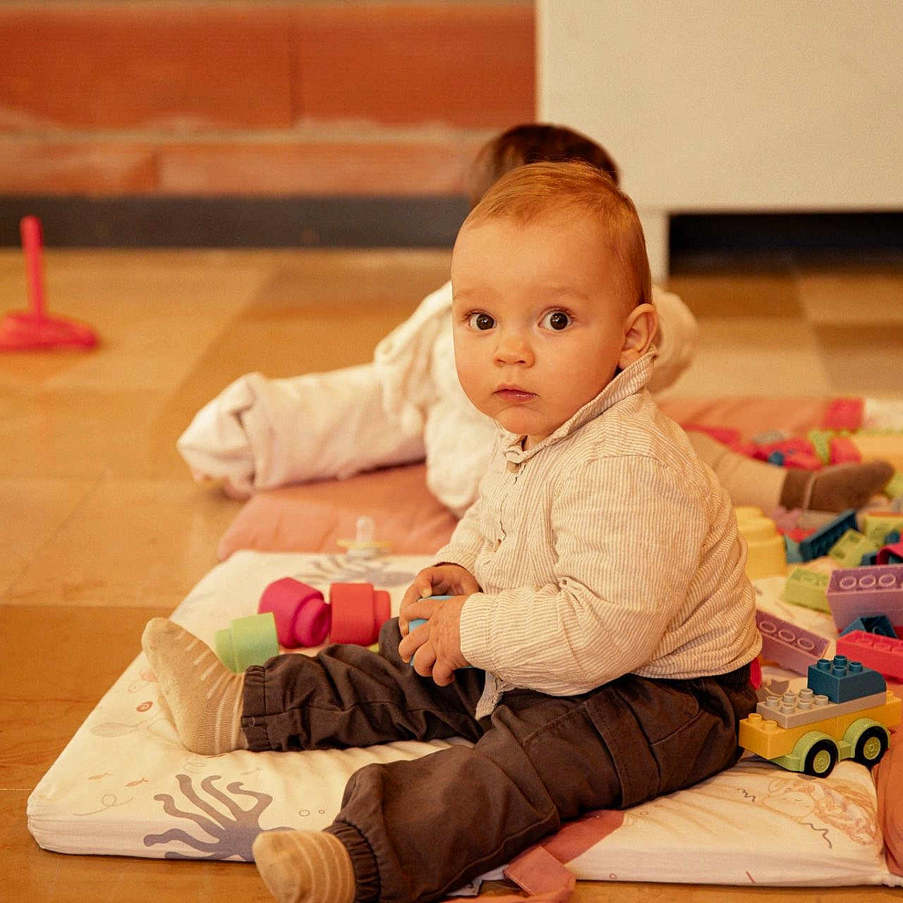 Nono a rejoint le concours — aidez-le/la à gagner de superbes lots ! baby, background, ball, building_blocks, casual_clothing, child, colorful, curious, floor, indoor, pants, person, play_mat, playtime, shirt, sitting, sock, soft_lighting, toys, young_child