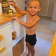 Waël a rejoint le concours — aidez-le/la à gagner de superbes lots ! toddler, child, barefoot, smiling, braid, kitchen, bell, cabinet, wood, countertop, jar, floor, home, interior, person, furniture, young_child, standing, cute, happy