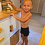 toddler, child, barefoot, smiling, braid, kitchen, bell, cabinet, wood, countertop, jar, floor, home, interior, person, furniture, young_child, standing, cute, happy