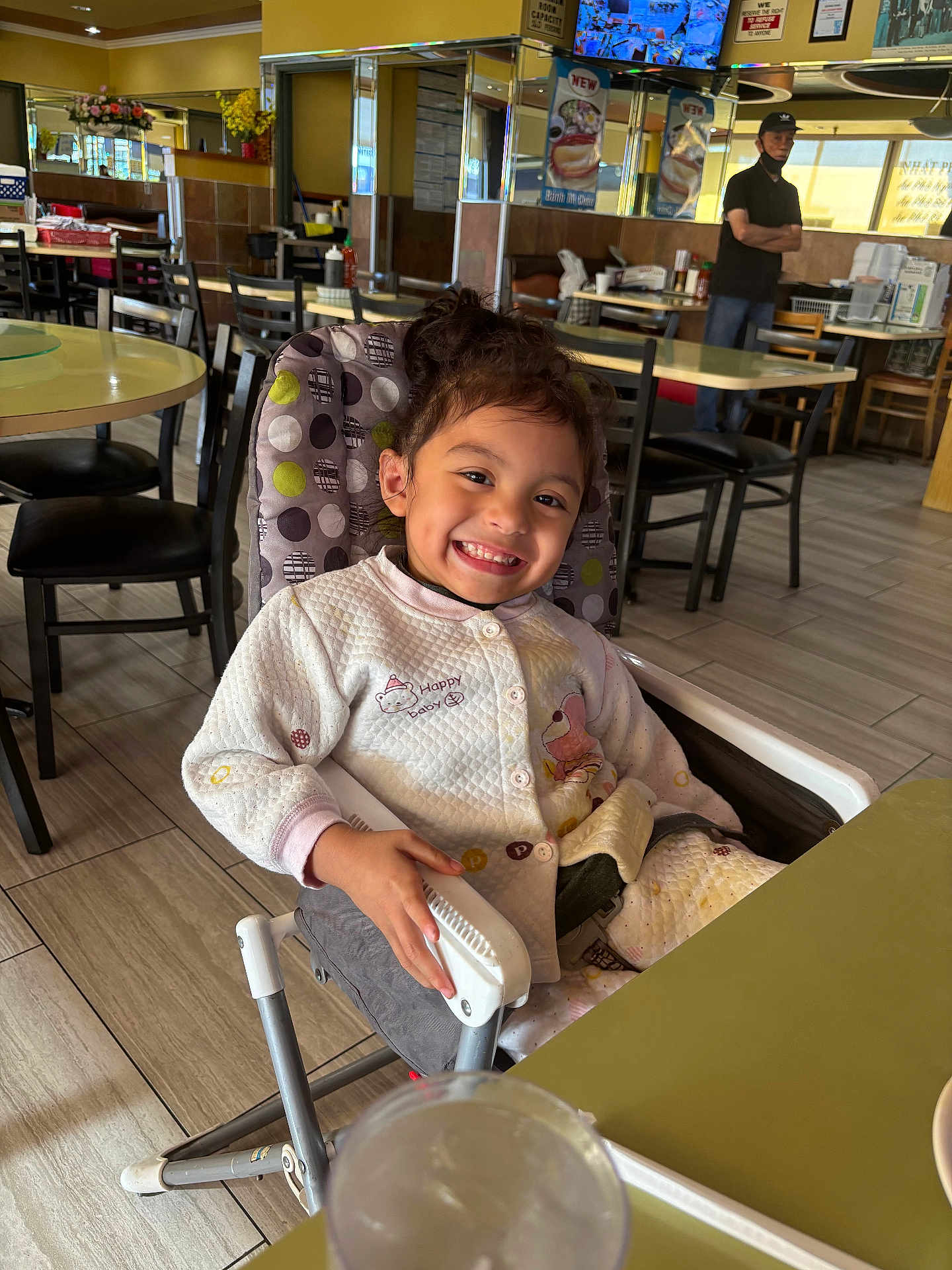 Jasmine joined the competition — help win amazing prizes! child, smiling, high_chair, restaurant, casual_clothing, indoor, table, chair, floor, man, background, window, tile_floor, person, happy, seat, furniture, dining, cute, portrait
