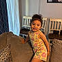 Jasmine joined the competition — help win amazing prizes! child, smiling, couch, indoor, curtain, chair, family_photo, wall, happy, person, furniture, home, patterned_pillow, flower_print, shorts, tank_top, brown_hair, curly_hair, playful, living_room