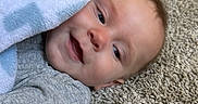 John joined the competition — help win amazing prizes! baby, infant, child, smiling, portrait, face, lying_down, blanket, gray_clothing, carpet, indoor, home, happy, eyes_open, head, pacifier, toy, floor, casual, close_up