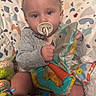John is registered to the contest to win money with this photo: baby, infant, child, pacifier, toy, colorful_toys, lying_down, blanket, patterned_blanket, portrait, face, blue_eyes, looking_at_camera, indoor, nursery, playtime, baby_clothing, hands, soft_lighting, happy