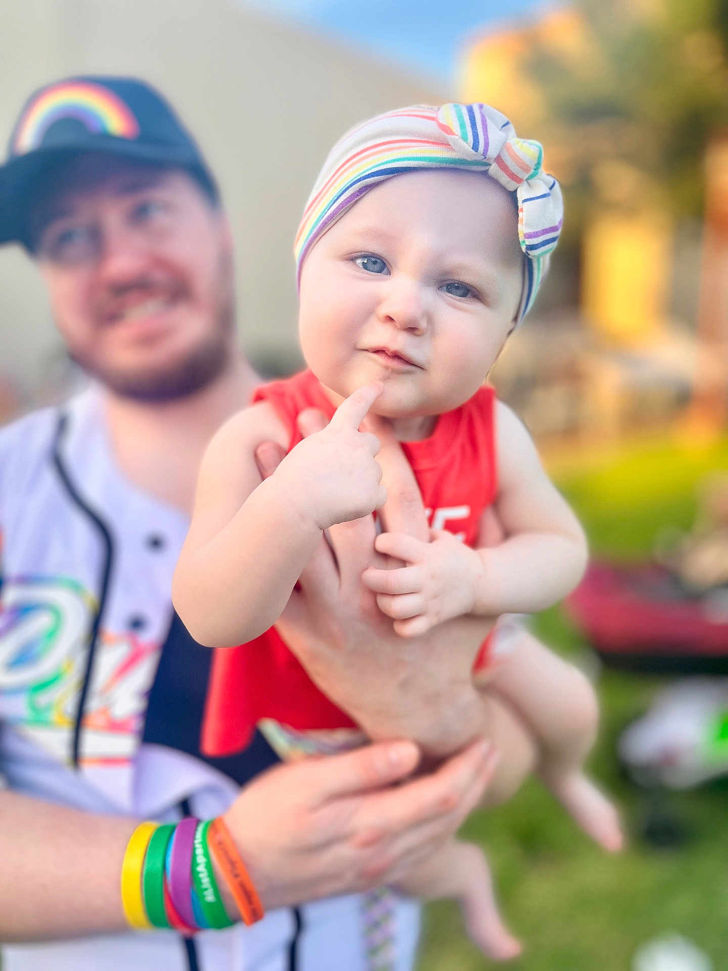 Dakoda joined the competition — help win amazing prizes! baby, child, adult, person, headband, rainbow, colorful, wristbands, red_clothing, outdoor, greenery, smiling, holding, portrait, face, hand, curious_expression, background_blur, sunlight, casual