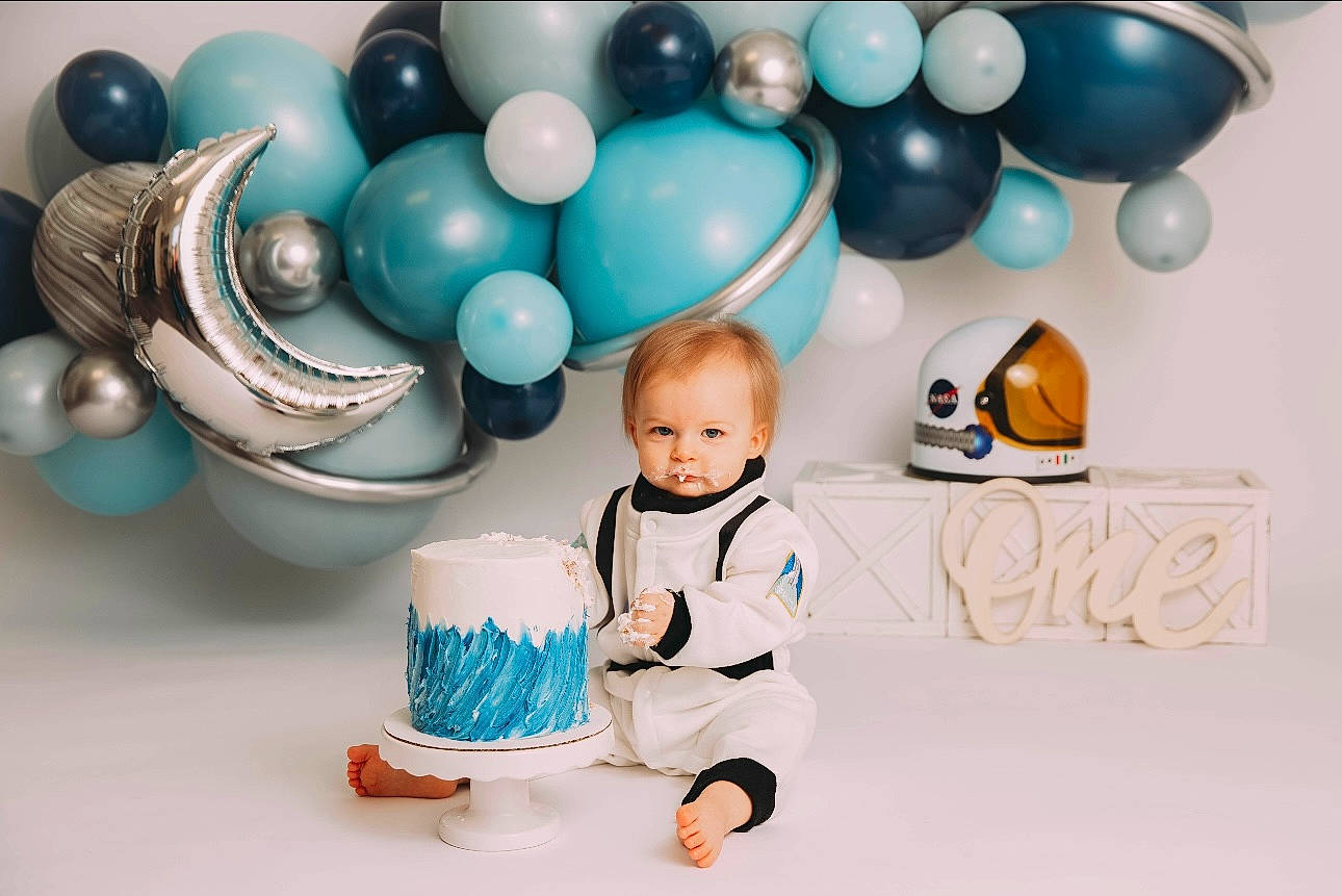 Benny is registered to the contest to win money with this photo: baby, baby_toddler_clothing, balloon, chair, child, circle, dishware, electric_blue, event, fashion_accessory, font, fun, happy, party, party_supply, pattern, person, porcelain, room, sitting