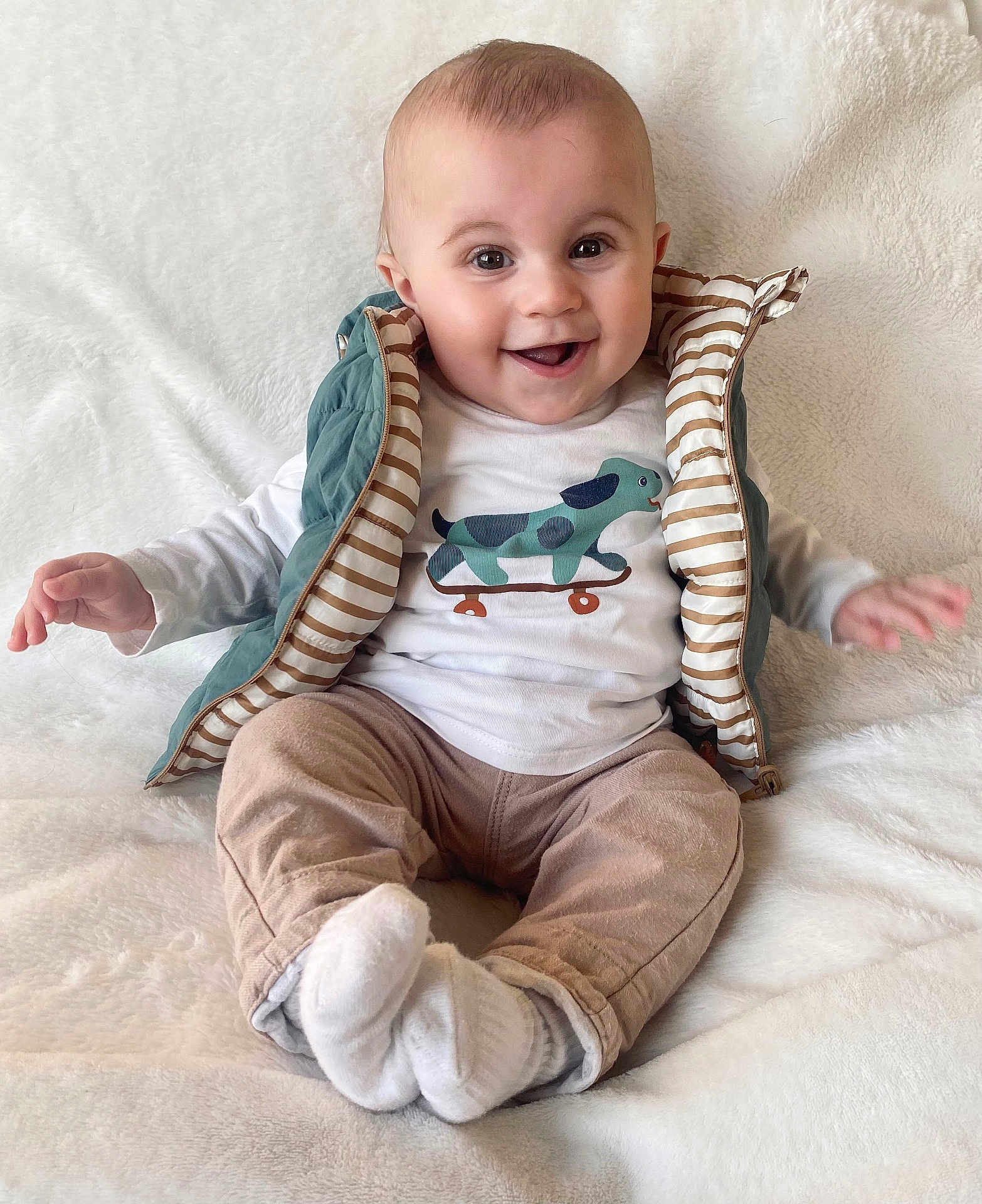 Clovis participe au concours pour gagner de l'argent avec cette photo : baby, child, clothing, cozy, cute, dog_graphic, face, happy, indoor, infant, pants, portrait, shirt, sitting, skateboard_graphic, smiling, socks, soft_texture, vest, white_blanket