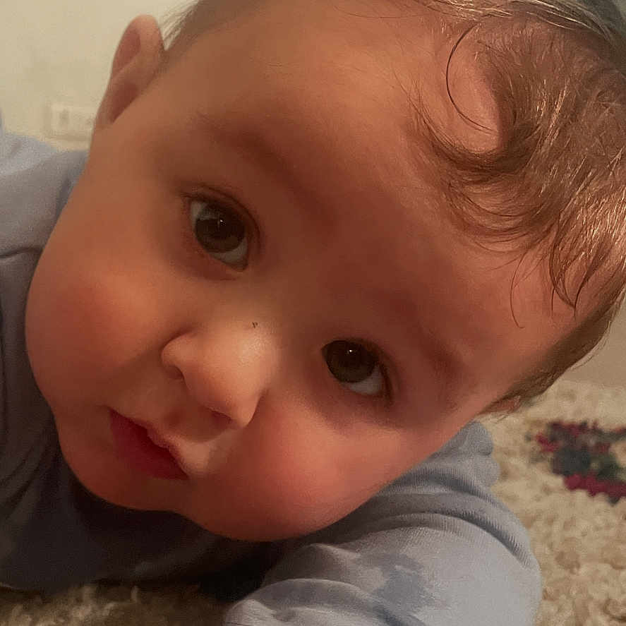 Anto Maria participe au concours pour gagner de l'argent avec cette photo : arm, baby, carpet, cheeks, close_up, cute, eyes, face, floor, forehead, gaze, hair, hand, indoor, infant, onesie, portrait, rug, sleepwear, tv_screen