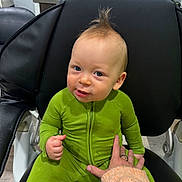 Kevin joined the competition — help win amazing prizes! baby, child, green_onesie, mohawk, chair, hand, indoor, person, seated, cute, smiling, fuzzy_sweater, playful, young_child, black_chair, floor, casual, portrait, human, expression