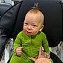 baby, child, green_onesie, mohawk, chair, hand, indoor, person, seated, cute, smiling, fuzzy_sweater, playful, young_child, black_chair, floor, casual, portrait, human, expression