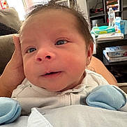 Pablo is registered to the contest to win money with this photo: baby, baby_wipes, blue_mittens, box, close_up, couch, cozy, curious, face, hand, home_interior, indoor, infant, newborn, person, portrait, shelf, sofa, table, water_bottle