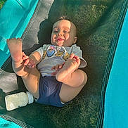 Domari is registered to the contest to win money with this photo: baby, child, smiling, feet, milk_bottle, outdoor, sunlight, mesh, teal, black, clothing, tshirt, shorts, grass, playful, infant, person, happy, relaxing, summer
