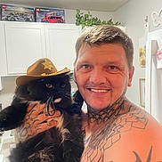Sylvester is registered to the contest to win money with this photo: animal_companion, black_cat, cabinets, cat, cowboy_hat, fluffy_cat, home, houseplant, indoors, kitchen, lego, long_hair, man, pet, portrait, selfie, sheriff_hat, smiling, tattoos, whiskers