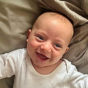 Finley is registered to the contest to win money with this photo: baby, smiling, face, infant, child, white_clothing, lying_down, blanket, soft_texture, happy, cute, closeup, skin, head, eyes, mouth, person, indoors, cozy, portrait