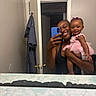 Lady is registered to the contest to win money with this photo: adult, baby, bathroom, mirror, selfie, smile, happy, child, tutu, pink, door, robe, phone, reflection, person, holding, hair, wall, door_knob, clothing
