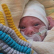 Siraj a rejoint le concours — aidez-le/la à gagner de superbes lots ! newborn, baby, infant, blanket, hat, nasal_cannula, oxygen_tube, knitted_toy, crochet, blue, yellow, gray, closeup, face, eyes, hospital, medical, cozy, wrapped, child