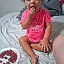 toddler, child, grapes, food, bed, pink_shirt, person, sitting, indoor, funny_face, snack, plate, barefoot, furniture, home, curly_hair, expression, casual, light, clothing