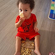 Nakaylia is registered to the contest to win money with this photo: barefoot, casual, child, curly_hair, floor, food, french_fries, home, indoor, looking_at_camera, messy, person, play_mat, popsicle, red_clothing, sitting, snack, toddler, wooden_floor, young_child
