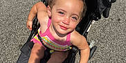Kmayrah joined the competition — help win amazing prizes! child, toddler, stroller, outdoor, sunlight, smiling, happy, colorful_clothing, footwear, sandals, pavement, black_stroller, person, summer, daylight, curly_hair, playful, seat, baby, casual
