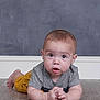 baby, child, infant, floor, gray_shirt, yellow_shorts, curious, lying_down, hands_clasped, indoor, wooden_floor, portrait, young_child, caucasian, head, face, eyes, expression, background, casual_clothing