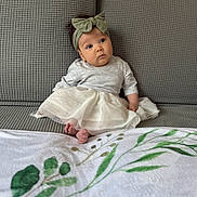 Chloe is registered to the contest to win money with this photo: baby, blanket, bow, child, clothing, couch, curious, cute, dress, foot, gray_couch, headband, indoor, infant, leaf_pattern, portrait, sitting, soft_lighting, texture, white_dress