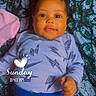 baby, infant, child, portrait, lying_down, looking_at_camera, brown_eyes, curly_hair, smiling, patterned_blanket, blue_clothing, long_sleeves, lightning_pattern, heart_graphic, sunday_text, time_text, indoor, close_up, candid, safe