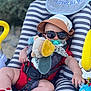 Tommy participe au concours pour gagner de l'argent avec cette photo : baby, sunglasses, hat, plush_toy, pacifier, baby_seat, striped_pattern, red_clothing, socks, outdoor, child, toy, summer, shade, relaxing, cute, infant, seat_belt, baby_accessories, playtime