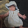 Kinsley is registered to the contest to win money with this photo: baby, infant, child, portrait, sitting, lying_down, bonnet, dress, plaid, blue, couch, sofa, cushion, indoor, home, arms_outstretched, bare_feet, face, clothing, relaxed
