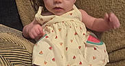 Kinsley is registered to the contest to win money with this photo: baby, infant, child, portrait, sitting, couch, indoors, watermelon, dress, floral_pattern, barefoot, smiling, wide_eyed, arms, legs, toes, cushion, furniture, cozy, photography