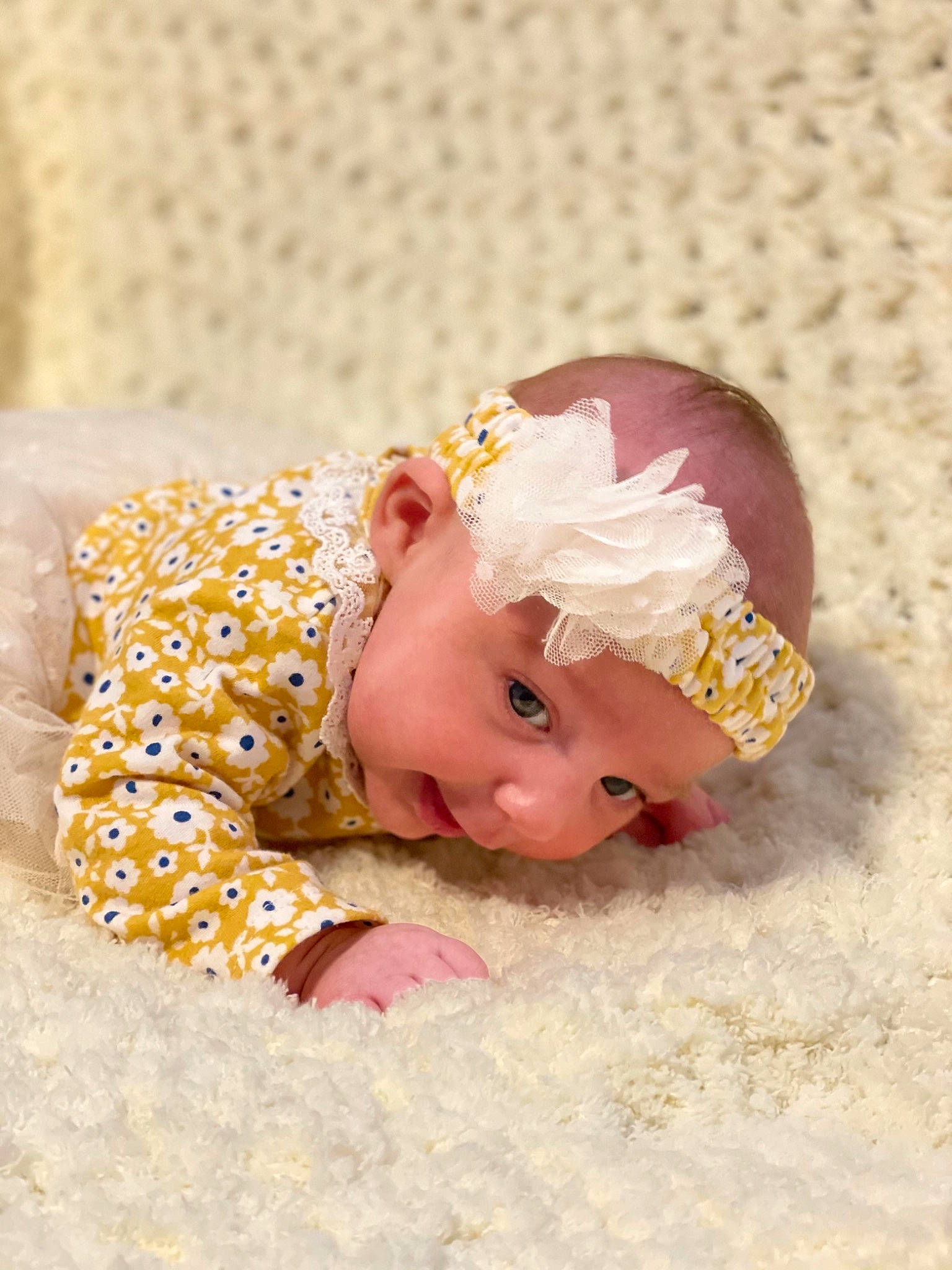 Kynlee is registered to the contest to win money with this photo: baby, baby_toddler_clothing, child, comfort, costume_accessory, fashion_accessory, flooring, grass, hair_accessory, happy, headband, headpiece, headwear, linens, magenta, pattern, peach, person, petal, pink