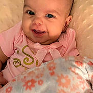 Jayda is registered to the contest to win money with this photo: baby, smiling, face, pink_clothing, blanket, floral_pattern, cute, infant, happy, portrait, child, cozy, indoors, head, skin, person, toddler, expression, warmth, comfort